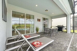 Een overdekt terras met een zwembad, ligbedden, een tafel en een barbecue.
