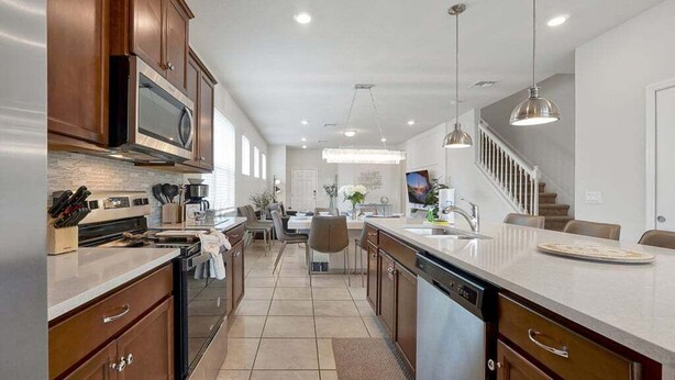 A modern kitchen with a central island, built-in appliances, and a dining area with a staircase. - Windsor Island Pool Home | Rare Backyard Privacy | 3 Master Suites | Game Room (Davenport)