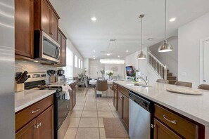 Una cocina moderna con una isla central, electrodomésticos integrados y una zona de comedor con una escalera.