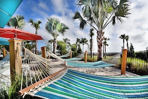 A hammock area with multiple hammocks and a red umbrella, surrounded by palm trees.