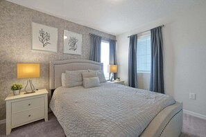 A bedroom with a bed, two bedside tables, wall art, and a window with curtains.