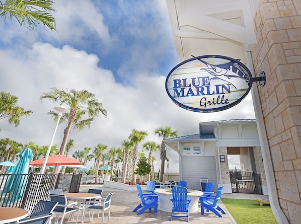 Un área de estar al aire libre con sillas Adirondack azules y un letrero que indica Blue Marlin Grill.
