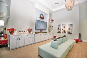 Una sala de estar moderna con un sofá azul claro, un televisor de pantalla plana montado en la pared, y una corona decorativa encima.