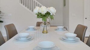 A dining table set with white plates and bowls, a vase with flowers, and a staircase in the background. - Windsor Island Pool Home | Rare Backyard Privacy | 3 Master Suites | Game Room (Davenport)