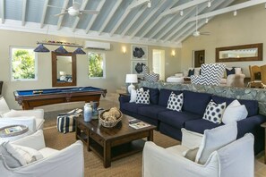 A living room with a pool table, a dark blue sofa with patterned cushions, and a stone accent wall. - Maria Bluff Main | Ocean Views & Pool | by BookVI (Cruz Bay)