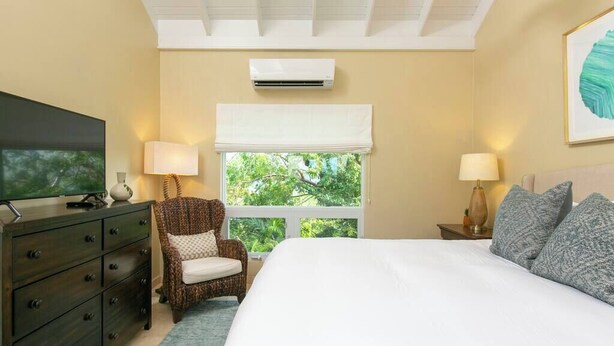 Hotelkamer met een bed, een televisie, een stoel, een nachtkastje en een raam met uitzicht op groen.
