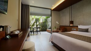 Habitación de hotel moderna con una cama grande, un escritorio con hervidor de agua, cafetera y una pequeña mesa con sillas. Se aprecia vista a zonas verdes desde la habitación.