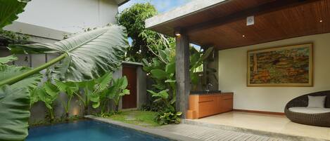 Piscina com deck de madeira, cercada por plantas tropicais.