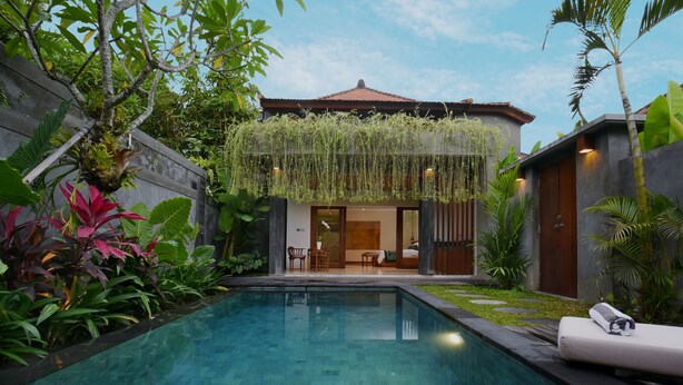 Una casa moderna con piscina, rodeada de abundante vegetación y un jardín cuidado.