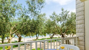 A balcony with a table set for breakfast, overlooking a coastal area with olive trees and a view of the sea.