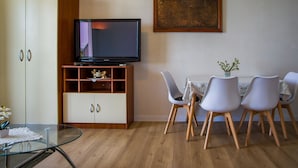 Un salon moderne avec un téléviseur à écran plat posé sur un meuble en bois, une table à manger avec quatre chaises et une table basse en verre.