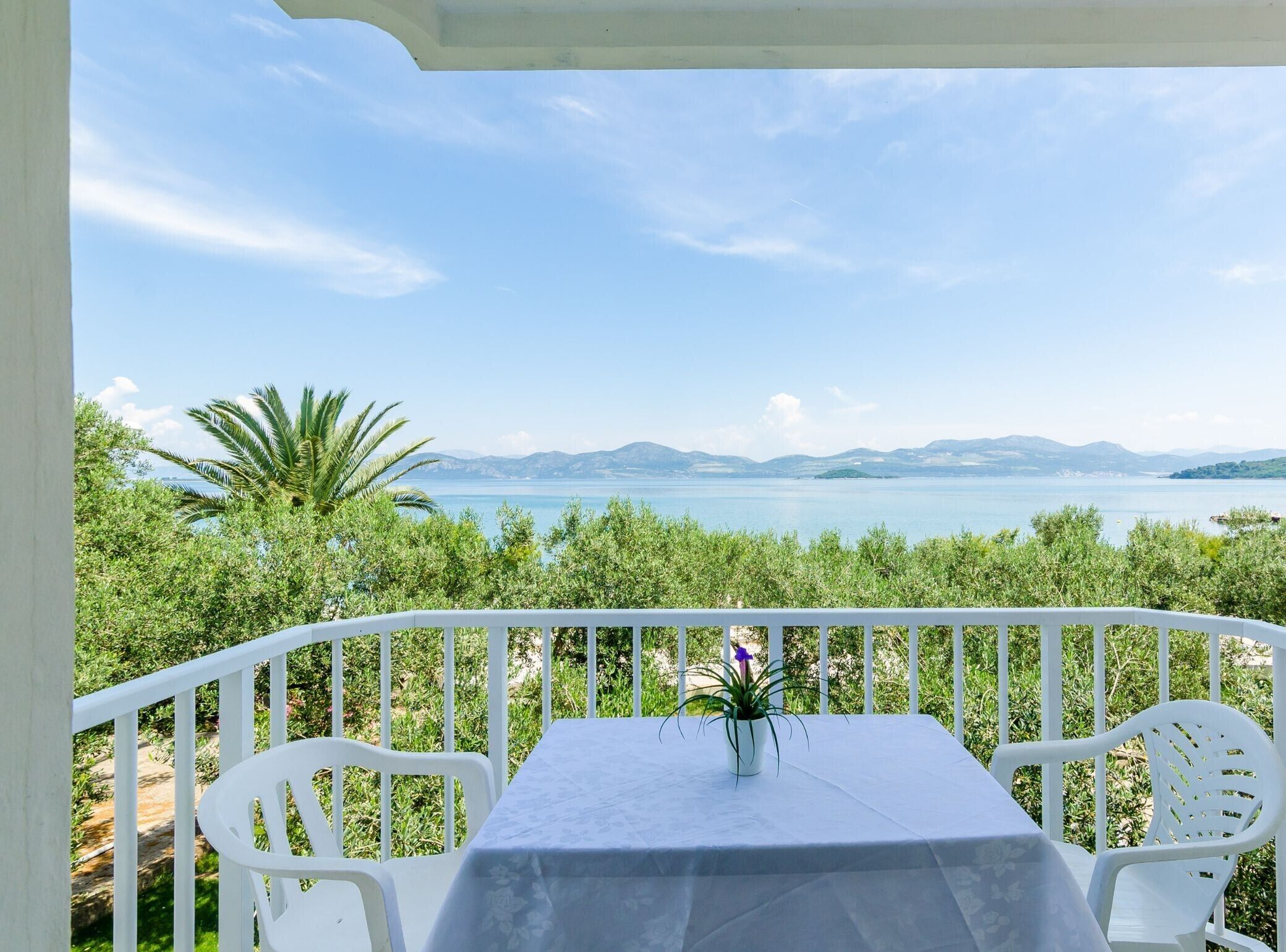 A balcony with a table and chairs overlooking a body of water and distant mountains.