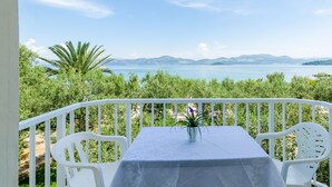 Un balcon avec une table et des chaises donnant sur une étendue d’eau et sur des montagnes lointaines.