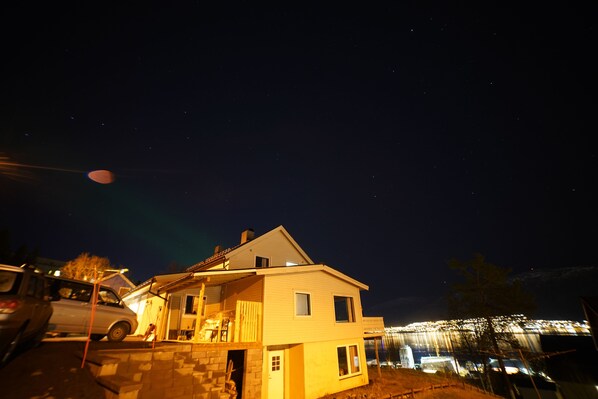 A two-story house with a garage, a driveway, and a large illuminated structure in the background. - Tor Appartment (Tromsø)