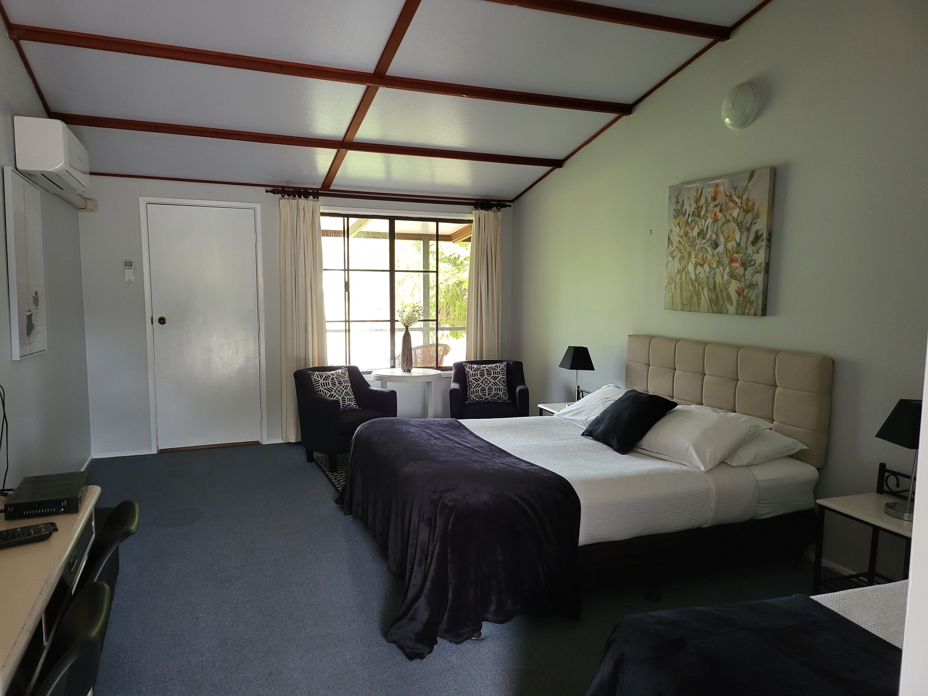 A hotel room with a bed, two armchairs, a small table, a lamp, and a painting on the wall.
