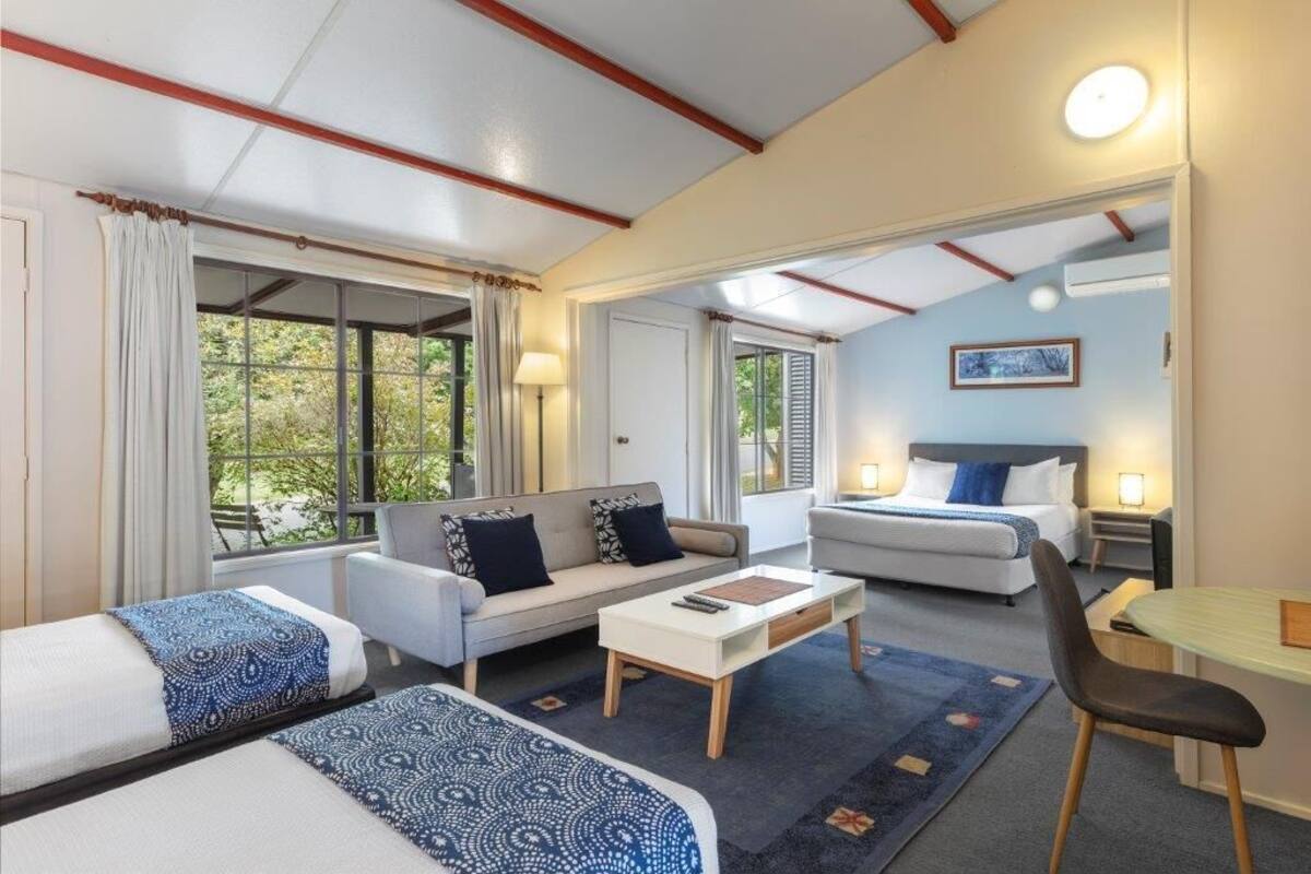A hotel room with a sofa, two single beds, a small table, and a chair.