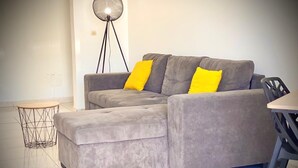 A grey sectional sofa with yellow cushions, a small round table, and a floor lamp in a modern living room. - ★ Sopraia Nature ★ New ✯ Countryside ✯ Calm (Les Abymes)