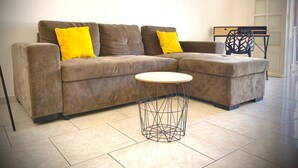 A L-shaped sofa with yellow cushions, a round wireframe coffee table, and a black metal chair in a room with tiled flooring. - ★ Sopraia Nature ★ New ✯ Countryside ✯ Calm (Les Abymes)