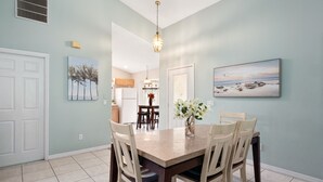 A dining area with a rectangular table, four chairs, a vase with flowers, a pendant light, and two wall-mounted paintings. - PROMO 5BR Villa with Pool/Spa, Near Disney - by Blue Sky Villas (Kissimmee)