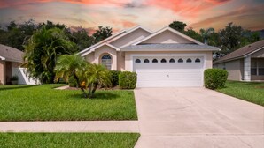 A single-story house with a garage, surrounded by well-maintained lawns and palm trees. - PROMO 5BR Villa with Pool/Spa, Near Disney - by Blue Sky Villas (Kissimmee)