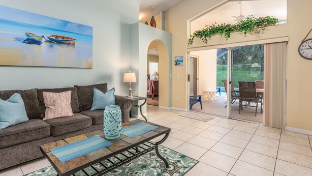 A living room with a sofa, coffee table, and a painting of boats on the wall. - PROMO 5BR Villa with Pool/Spa, Near Disney - by Blue Sky Villas (Kissimmee)