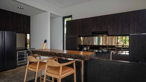 Eine moderne Küche mit dunklen Holzschränken, einer großen Kochinsel mit Barhocker, Edelstahlgeräten und Blick ins Freie.