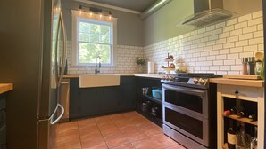 Eine Küche mit einem Edelstahl-Kühlschrank, einem Doppelbackofen, einer Spüle mit Fenster darüber und einer gefliesten Spritzschutzwand.