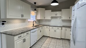 Uma cozinha com armários brancos, bancadas de granito e piso cerâmico.