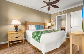 Habitación de hotel con cama, dos mesitas de noche con lámparas, ventilador de techo y puerta que da a otra habitación.