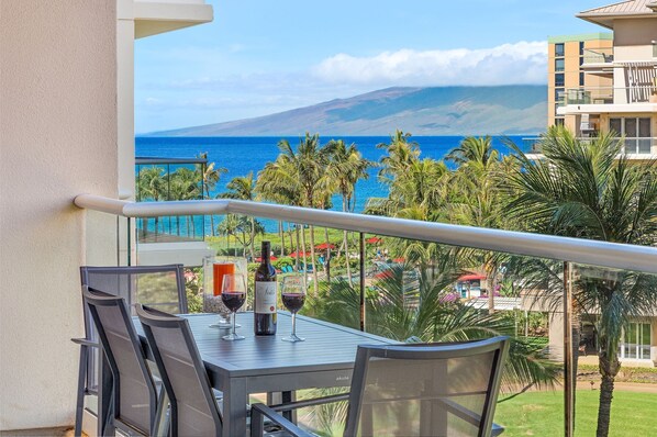 Un balcón con una mesa preparada para dos, con vistas a la costa, palmeras y una montaña en la distancia.