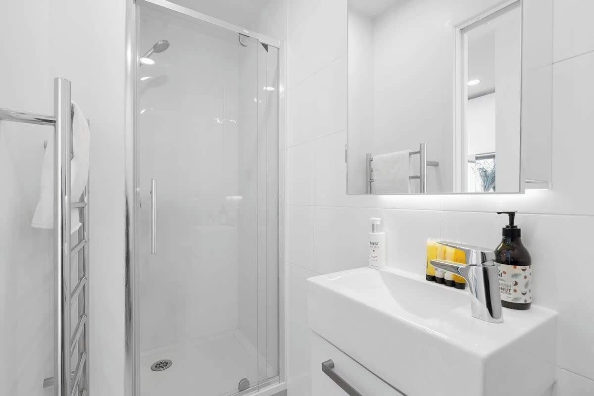 A modern bathroom with a glass shower enclosure, a white sink with a mirror above it, and toiletries on the counter.