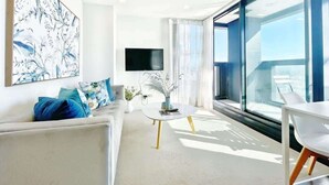 Una sala de estar moderna con un ventanal grande, un televisor de pantalla plana y un sofá blanco con cojines azules.