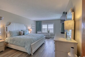 Une chambre à coucher comprenant un lit, des tables de chevet, une commode, un miroir et une fenêtre avec des stores.