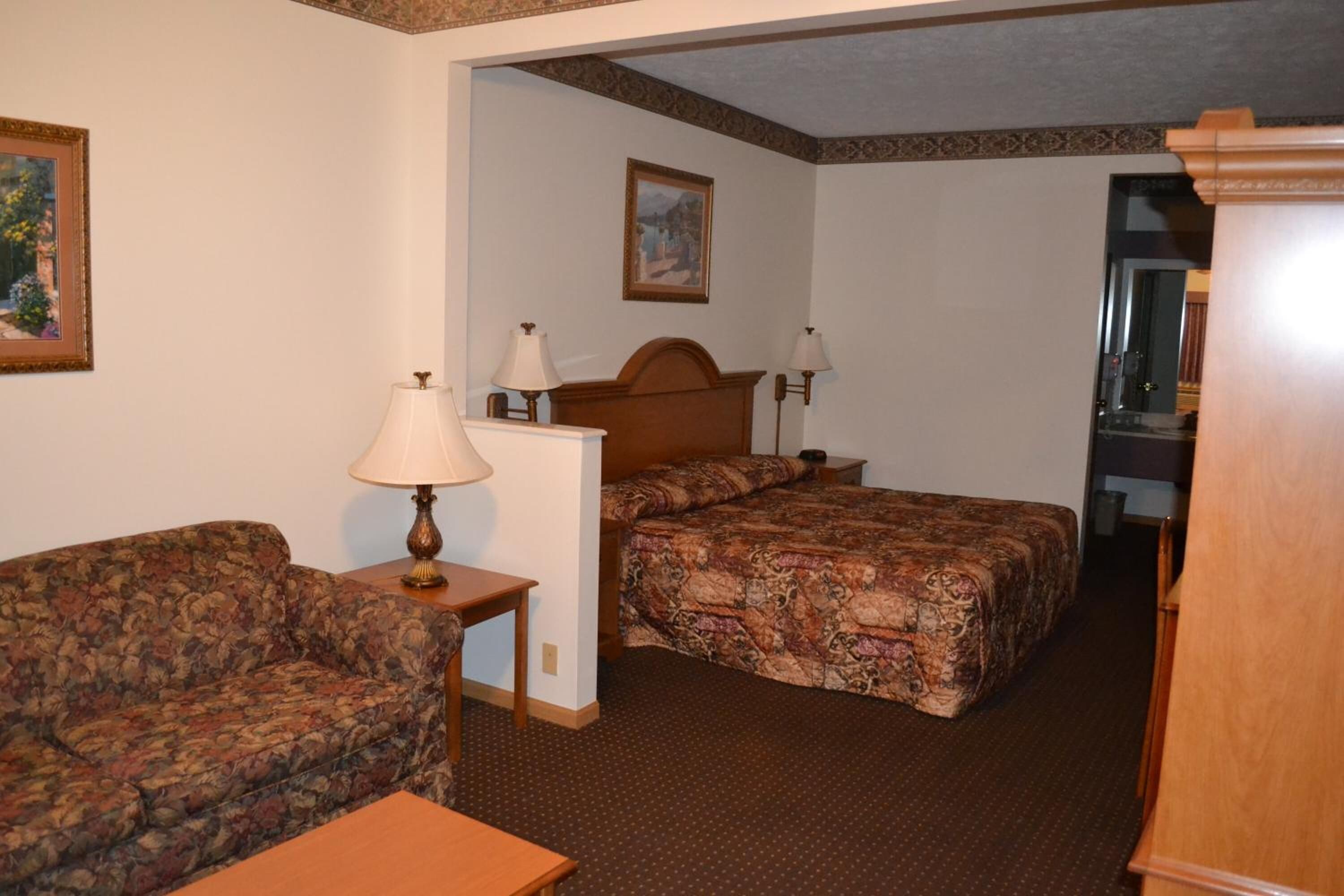 Una habitación de hotel con una cama, un sofá, dos lámparas y un cuadro en la pared.