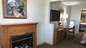 Quarto de hotel com lareira, televisão fixada na parede, secretária com cadeira e tapete estampado.