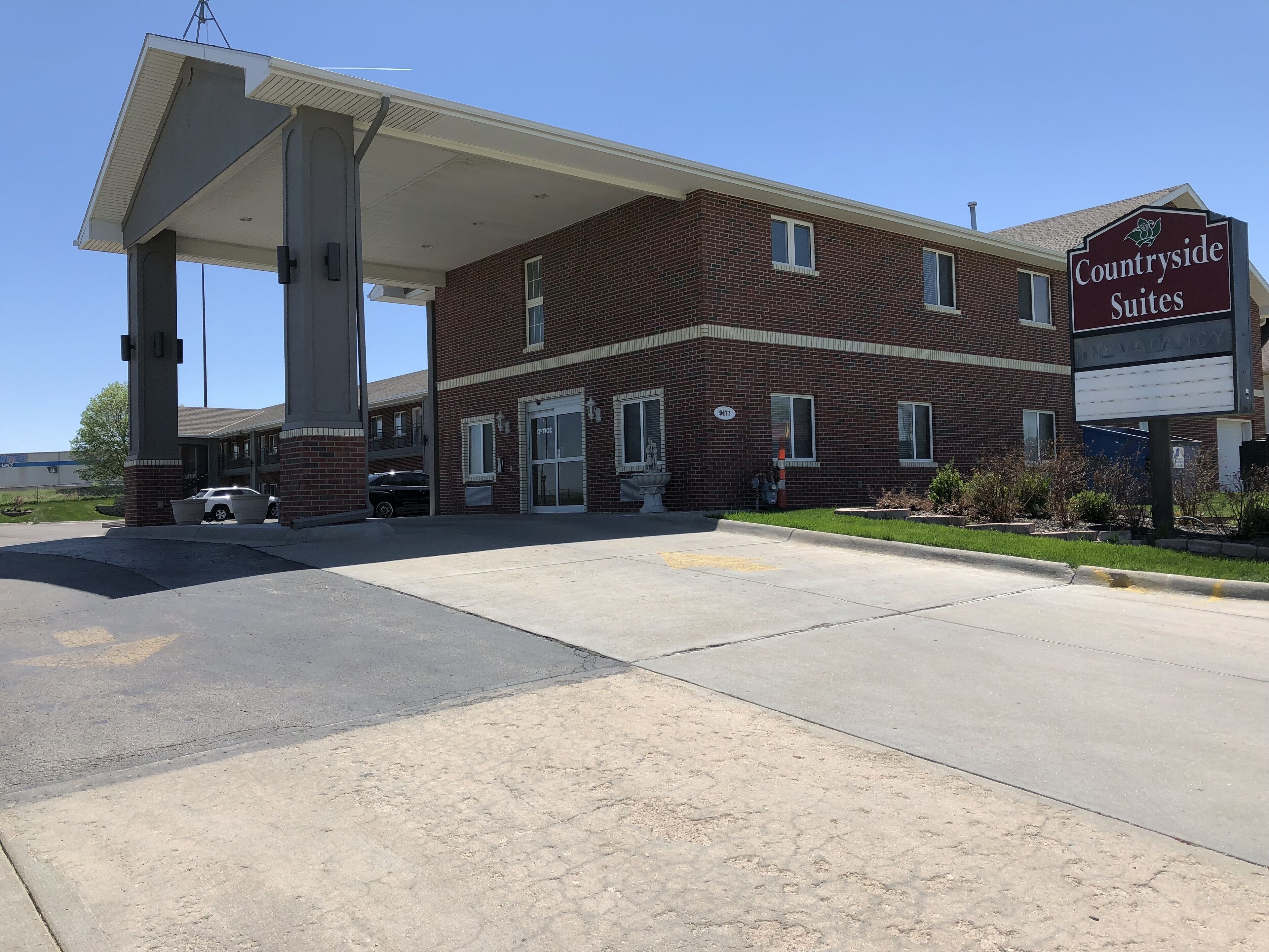 A brick building with a sign for Countryside Suites, a covered parking area, and a clear sky.