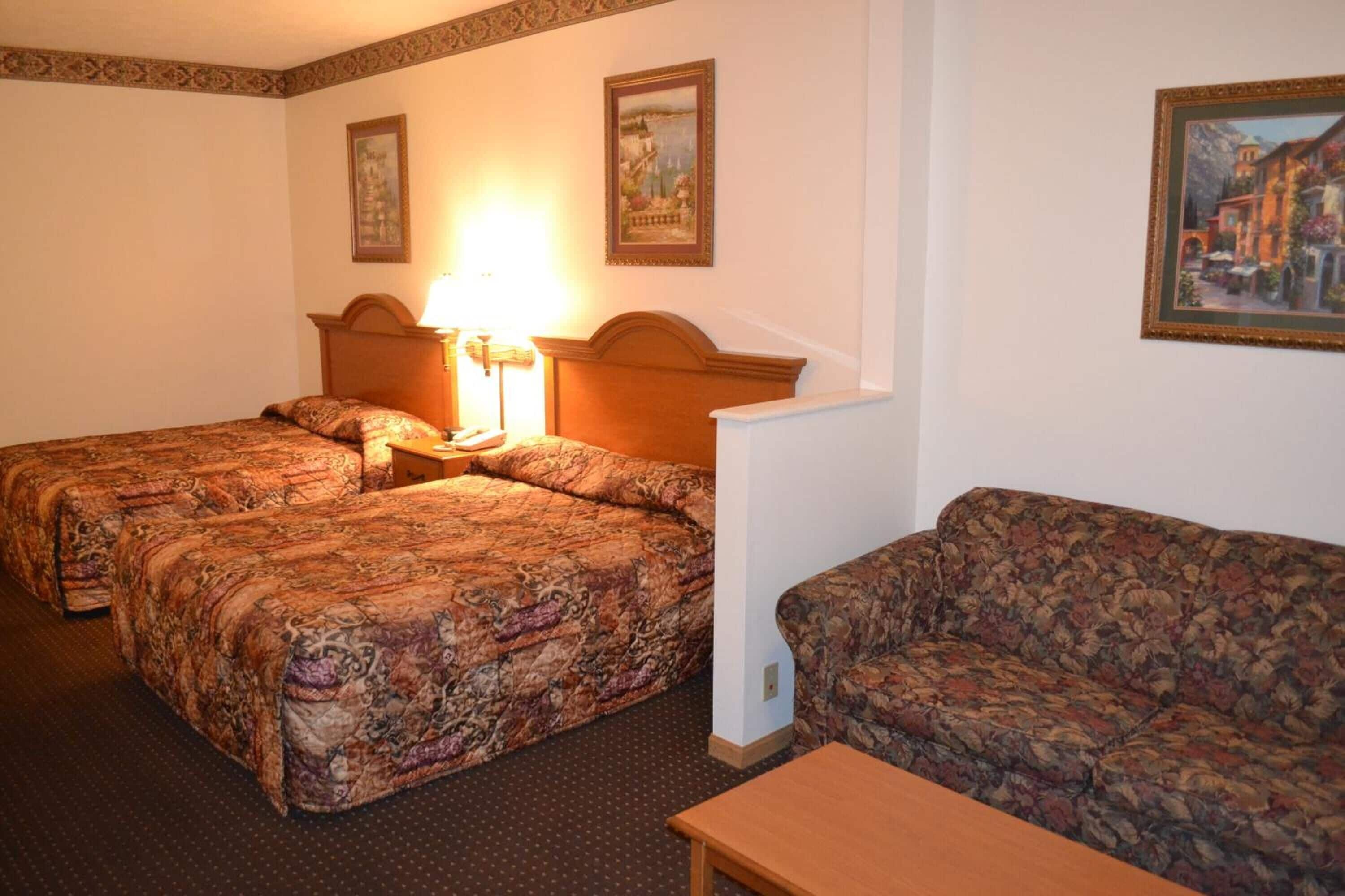 Een hotelkamer met twee bedden, een bank, een nachtkastje met lamp en ingelijste foto's aan de muur.