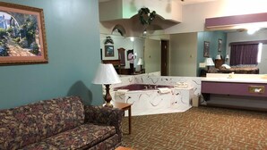 Uma sala de estar com sofá floral, mesa de centro de madeira, espelho grande, banheira e banheiro com pia e espelho.