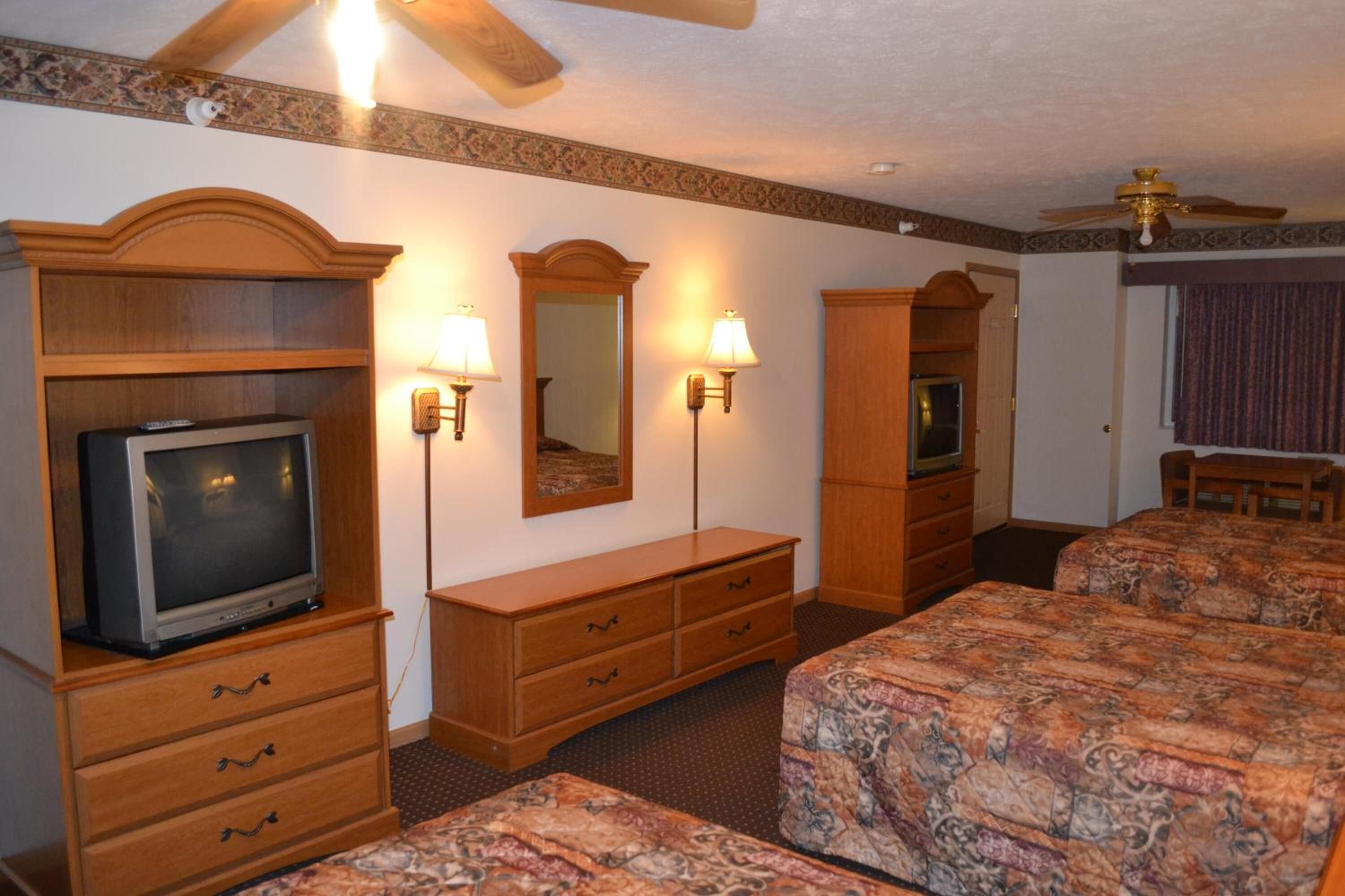 A hotel room with a television, two bedside tables, a dresser, a mirror, and a ceiling fan.
