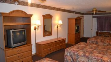 A hotel room with a television, two bedside tables, a dresser, a mirror, and a ceiling fan.
