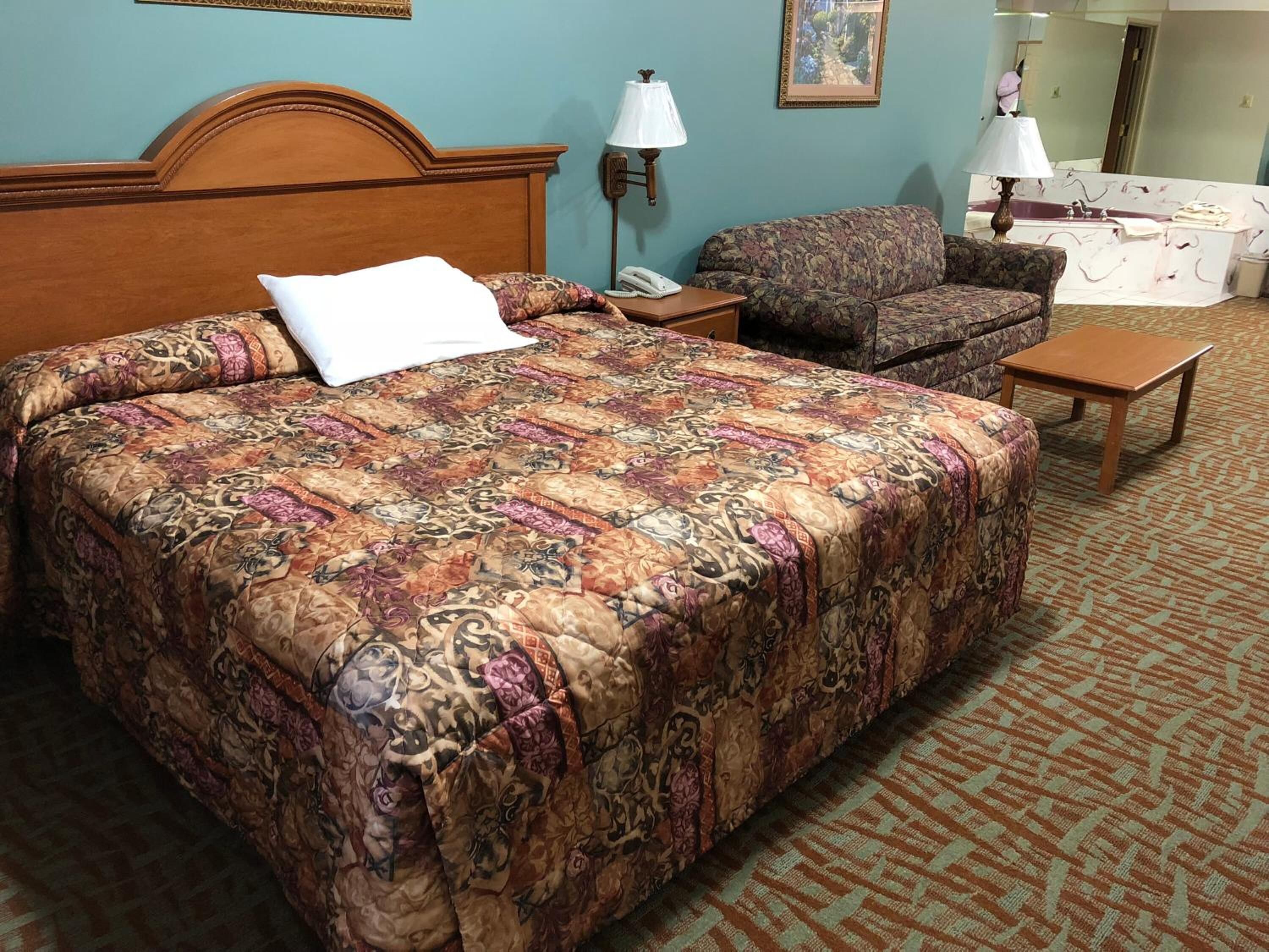 A hotel room with a large bed, a sofa, a nightstand, a lamp, and a small table.