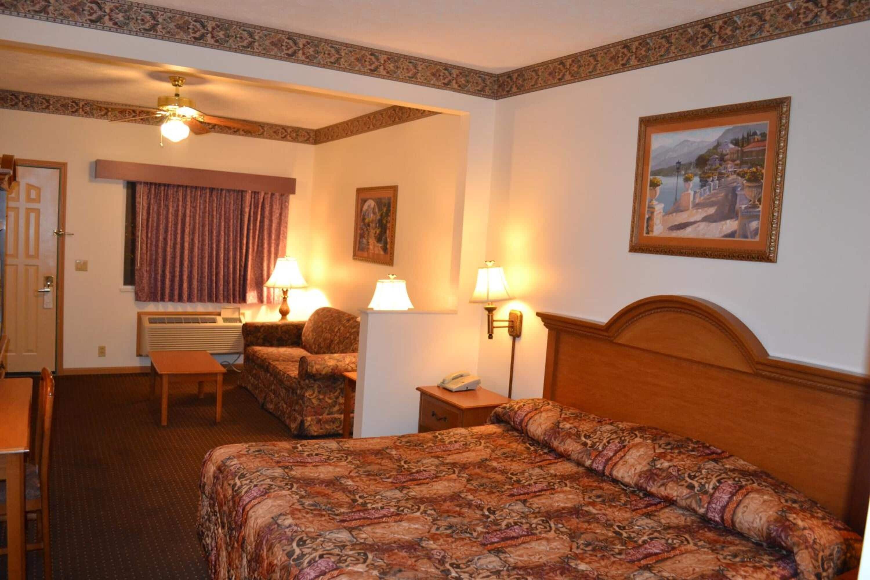 Een hotelkamer met een bed, een bank, een bureau en een stoel. Er hangt een schilderij aan de muur en er is een plafondventilator.