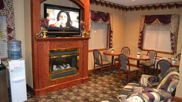 A living room with a fireplace, a television, a water dispenser, and a dining area with chairs and a table.