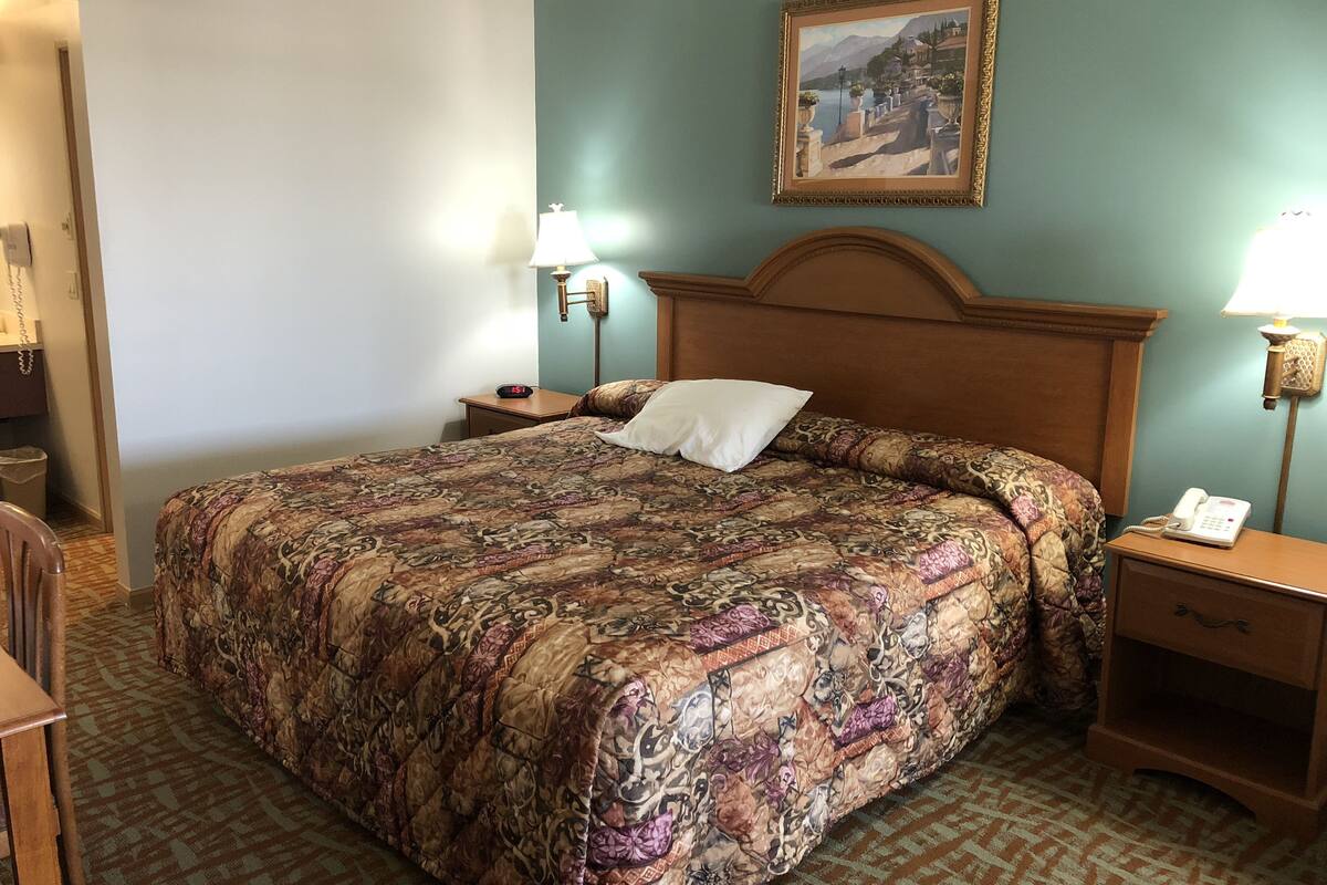 Una camera d'albergo con un letto grande, due comodini, una poltrona e un quadro appeso al muro.