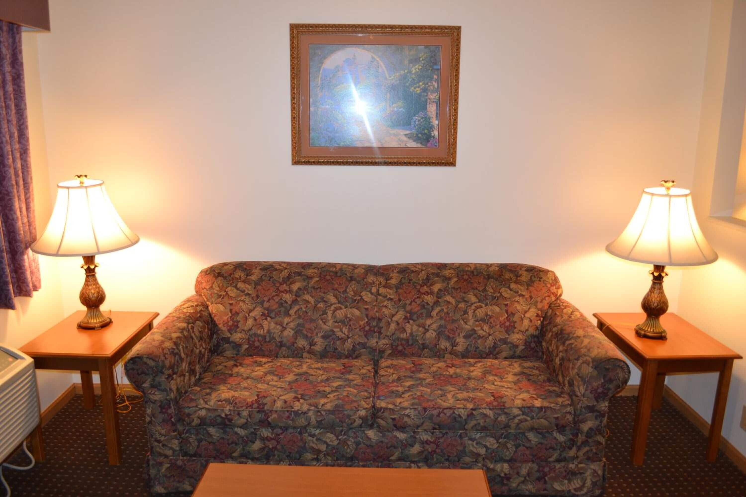 A room with a floral sofa, two lamps on side tables, and a framed picture on the wall.