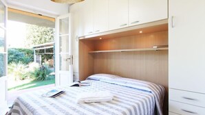 Une chambre à coucher comprenant un lit, une table de chevet, une armoire et donnant sur un jardin.