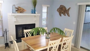 A dining area with a wooden table and white chairs, a white brick fireplace, and decorative fish on the wall.