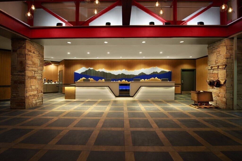 Un hall d’entrée spacieux avec un comptoir d’accueil, des piliers en pierre et une grande fresque murale.