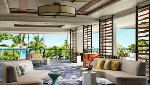 Un salon moderne doté d’une grande fenêtre donnant sur un paysage tropical, comprenant un canapé, des fauteuils et une table basse.