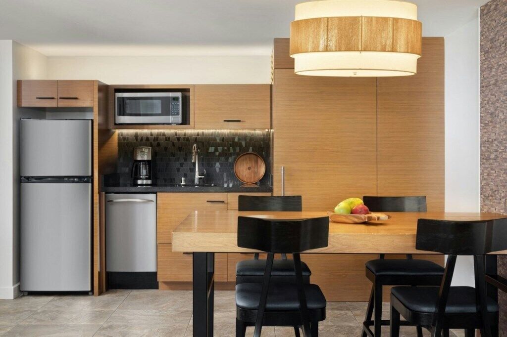 A modern kitchen with a built-in microwave, stainless steel refrigerator, and a wooden dining table with black chairs.